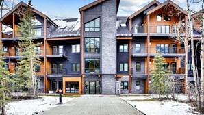 A multi-story hotel with a central entrance, balconies, and a snowy landscape. - 3 Bedroom with Outdoor Heated Pool and Hottub! (Canmore)