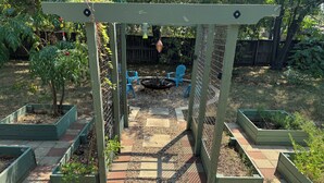 Een tuinpati met verhoogde plantenbakken, een pergola en een vuurkuil.