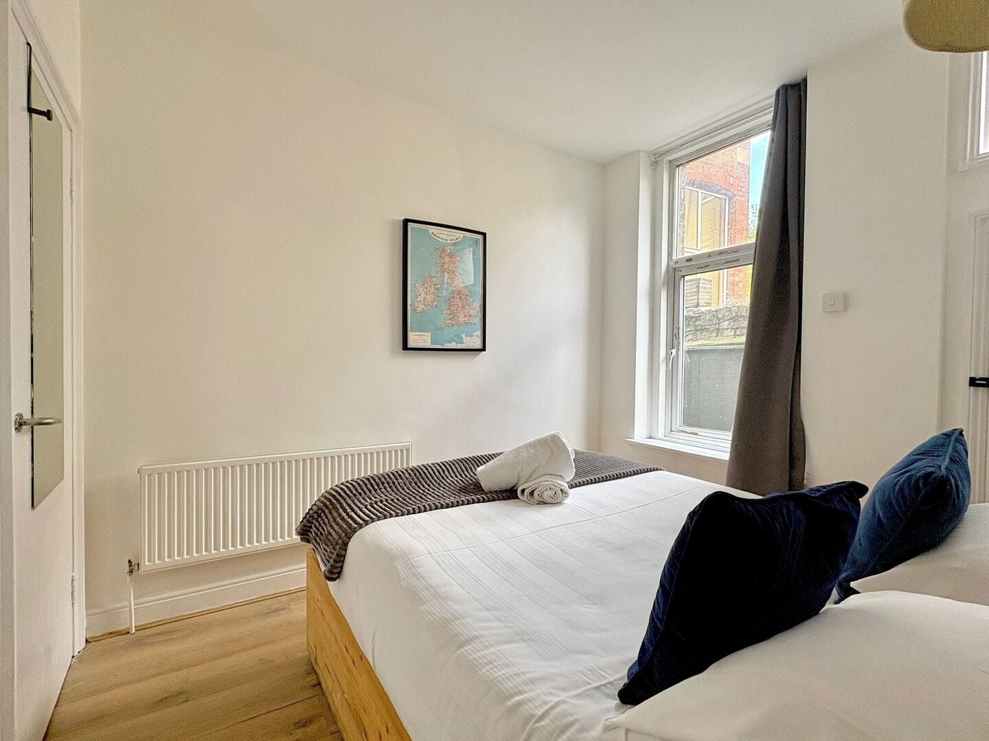Une chambre à coucher avec un lit, un radiateur, une fenêtre avec des rideaux et un tableau encadré au mur.