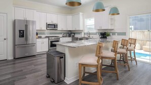 A modern kitchen with white cabinets, stainless steel appliances, a central island with bar stools, and pendant lighting. - Family Beach Escape w/ Private Pool|Downtown St. A (St. Augustine)