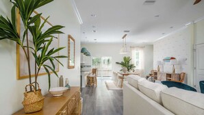 A spacious living area with a sofa, dining table, and chairs, a large plant, and a wooden cabinet with baskets. - Family Beach Escape w/ Private Pool|Downtown St. A (St. Augustine)