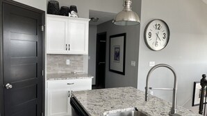 A kitchen with white cabinets, a granite countertop, a stainless steel sink, and a wall clock. - 2 Story cabin at Bridges Bay Resort comes w/6 daily waterpark passes! (Arnolds Park)
