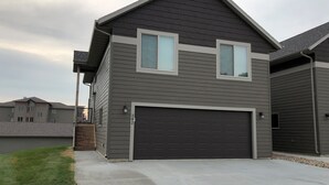 A two-story house with a dark gray exterior, a garage, and a small front porch. - 2 Story cabin at Bridges Bay Resort comes w/6 daily waterpark passes! (Arnolds Park)