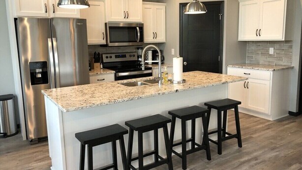 A modern kitchen with white cabinets, stainless steel appliances, a granite countertop, and black bar stools. - 2 Story cabin at Bridges Bay Resort comes w/6 daily waterpark passes! (Arnolds Park)