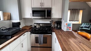 Una cocina compacta con gabinetes blancos, un microondas de acero inoxidable, una cocina a gas y una encimera de madera.