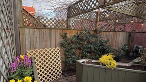 Una terraza de madera con una estructura de celosía en la parte superior, rodeada por una valla de madera y un muro de ladrillo.