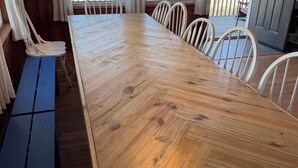 A wooden dining table with chairs, a bench, and a view of the ocean through large windows. - Surf City Oceanfront -6BR -2.5 Bath -Sleeps 12 -Direct Beach Access (Surf City)