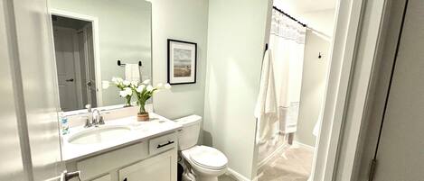 A bathroom with a white sink, mirror, and toilet. There is a framed picture on the wall and a towel rack.