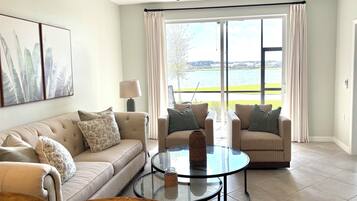 A living room with a beige sofa, two armchairs, a glass coffee table, and a ceiling fan.