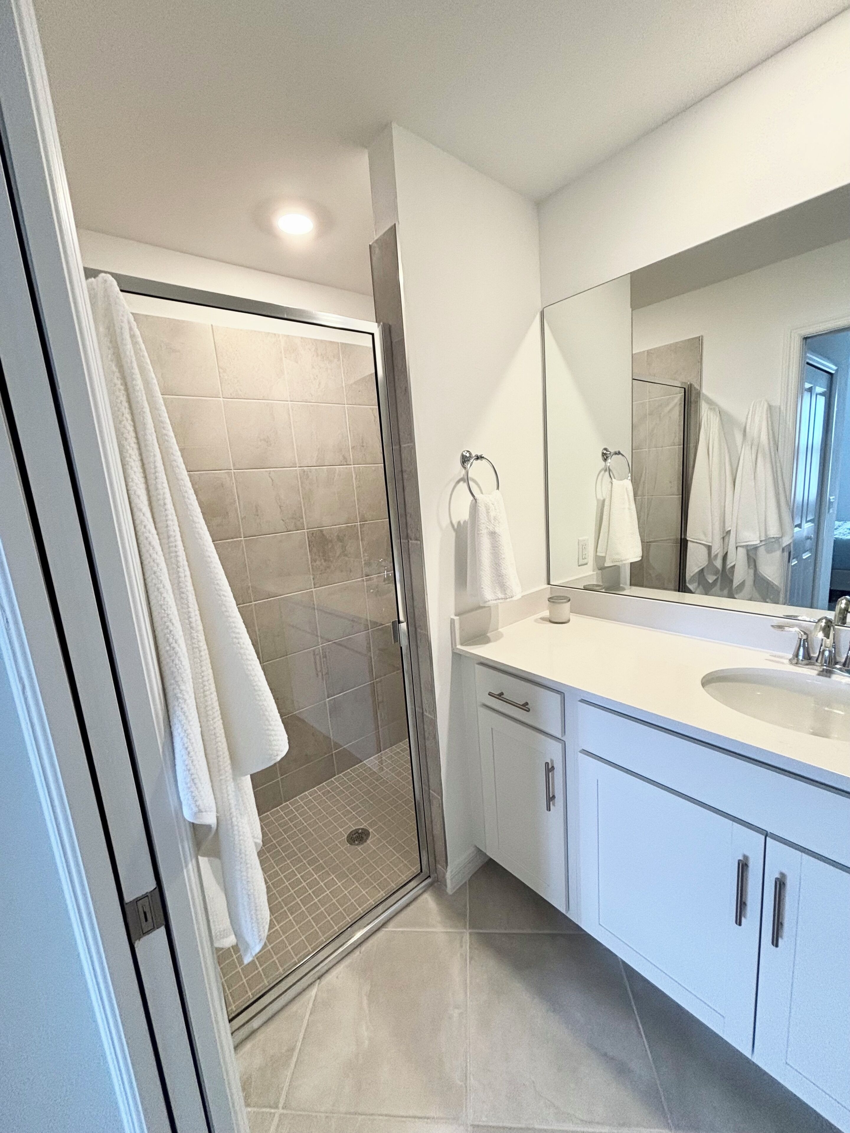 A modern bathroom with a glass-enclosed shower, a large mirror, and white cabinetry.