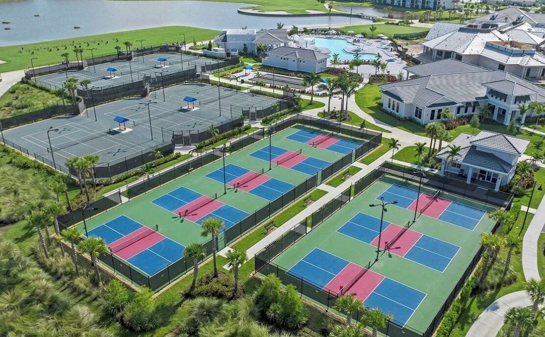 An aerial view of a residential area with multiple tennis courts, a swimming pool, and houses.