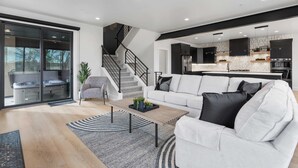 A modern living room with a white sofa, a coffee table, and a staircase leading to a kitchen. - Classy Corner Retreat | Hot Tub + Fireplace (Fort Collins)