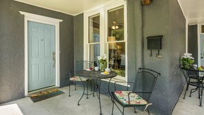 Un porche techado con una mesa y sillas, una puerta azul y un ventanal con vistas al interior.
