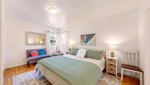 Un dormitorio con una cama, un banco, una mesita de noche, un espejo y un cuadro.