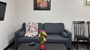 A modern living room with a sofa, a coffee table with a vase of flowers, a TV mounted on the wall, and two chairs.