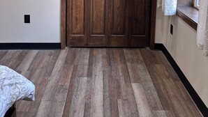 A room with a large wooden wardrobe, a window with patterned curtains, and a wooden floor.