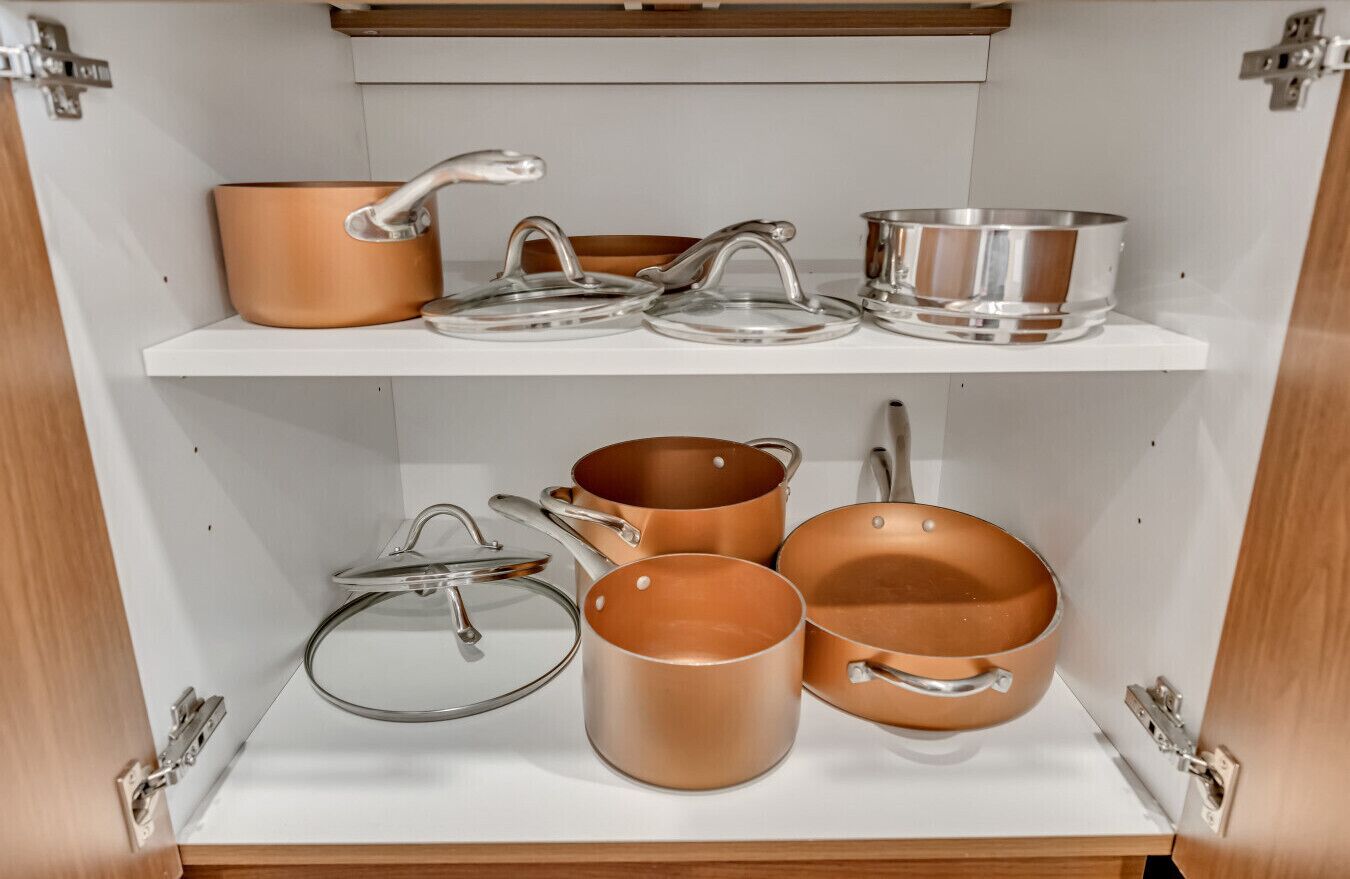 A kitchen cabinet with copper cookware and stainless steel lids.