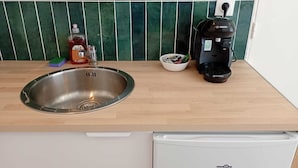 Eine Küche mit einer Spüle aus Edelstahl, einer Kaffeemaschine, einer Flasche rote Flüssigkeit und einer Schale mit Stiften.