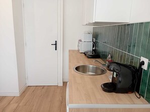 Eine kleine Küchenzeile mit Spüle aus Edelstahl, einer Kaffeemaschine, einem Wasserkocher und einem Toaster.