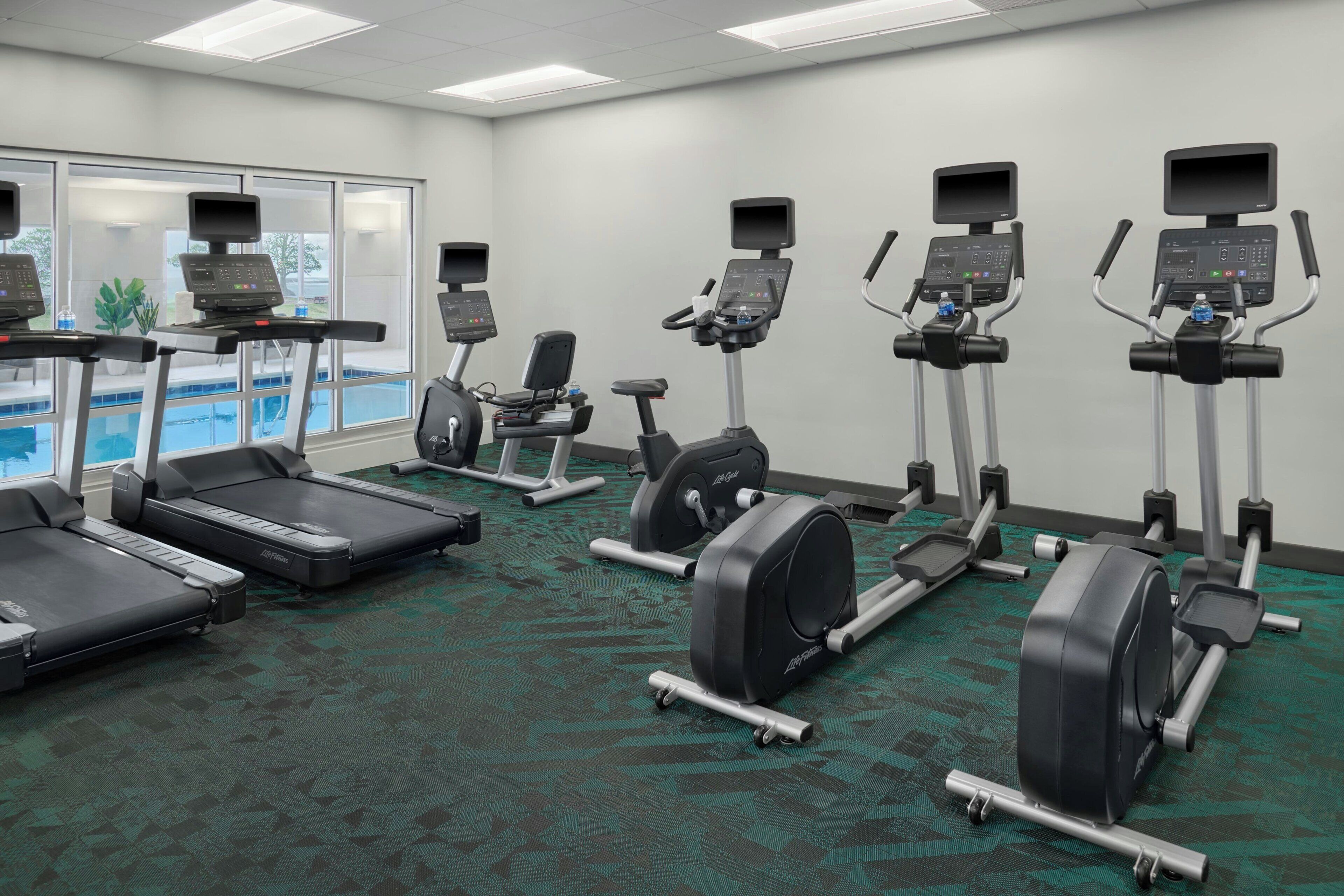 A gym with treadmills, elliptical machines, and a pool view.