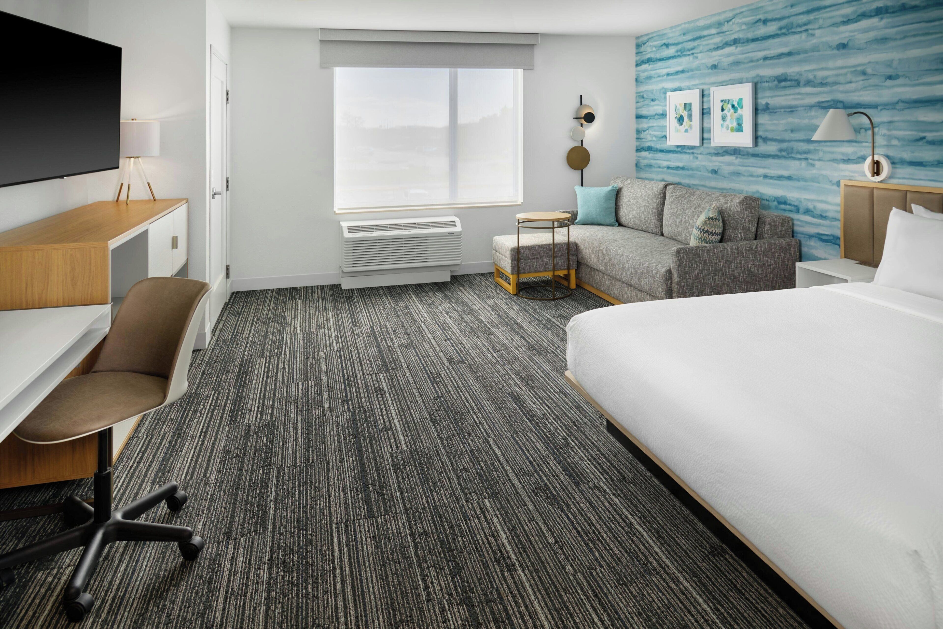 A hotel room with a bed, a desk, a chair, a sofa, a small table, and a wall-mounted TV.