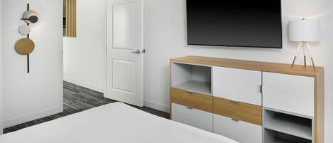 Ein Hotelzimmer mit einem Bett, einem an der Wand befestigten Fernseher, einem Holzschrank und einer Tür zu einem weiteren Raum.