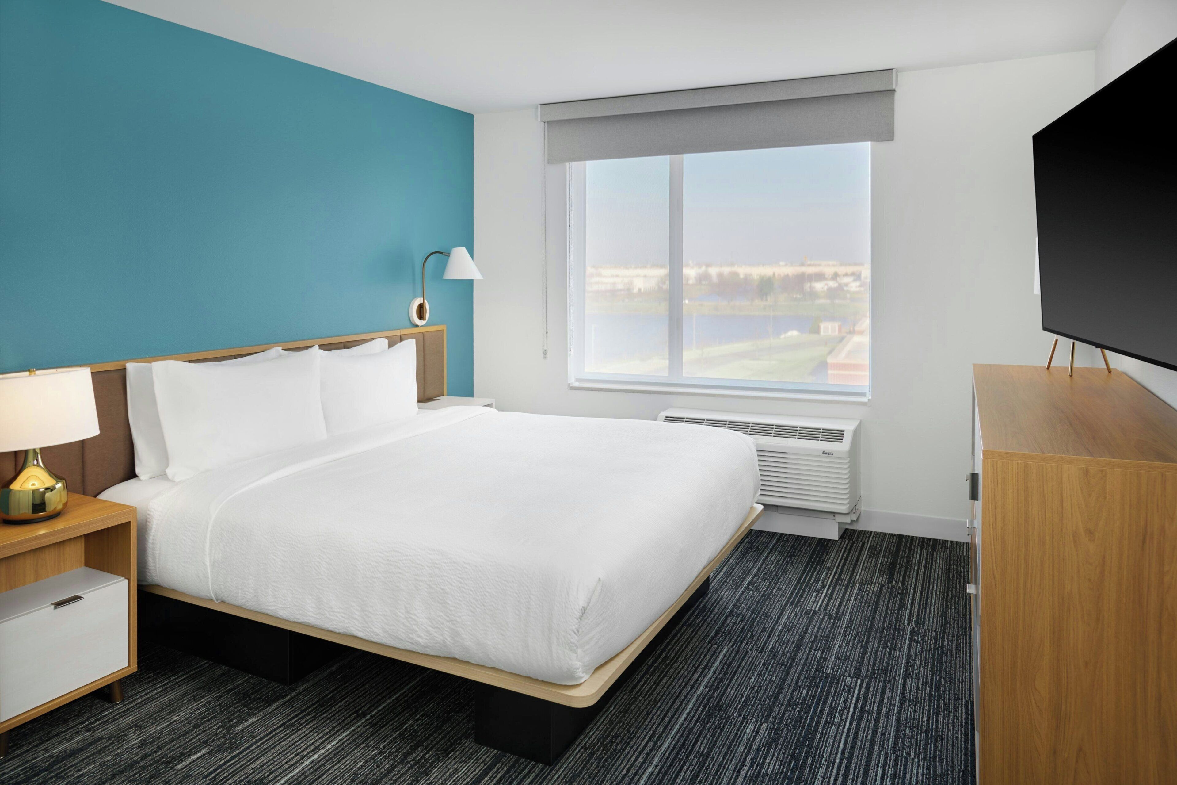 A hotel room with a bed, a TV, a window with a view, and a desk with a lamp.