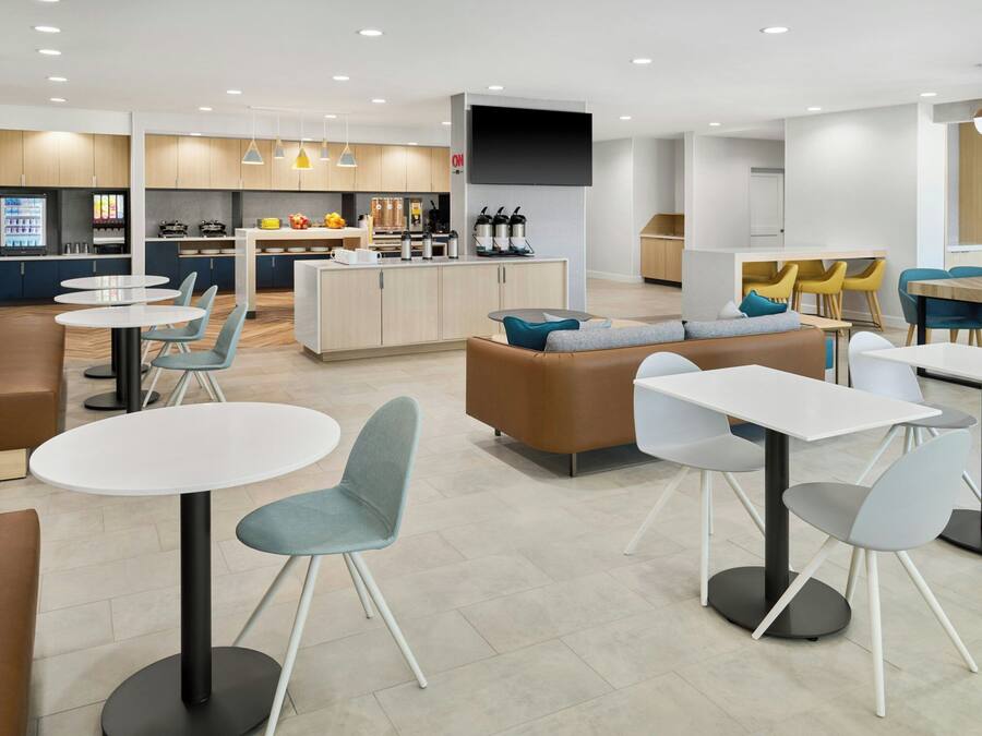 Eine moderne Hotelhalle mit runden Tischen, Sofas und einer zentralen Insellounge mit Küchengeräten.