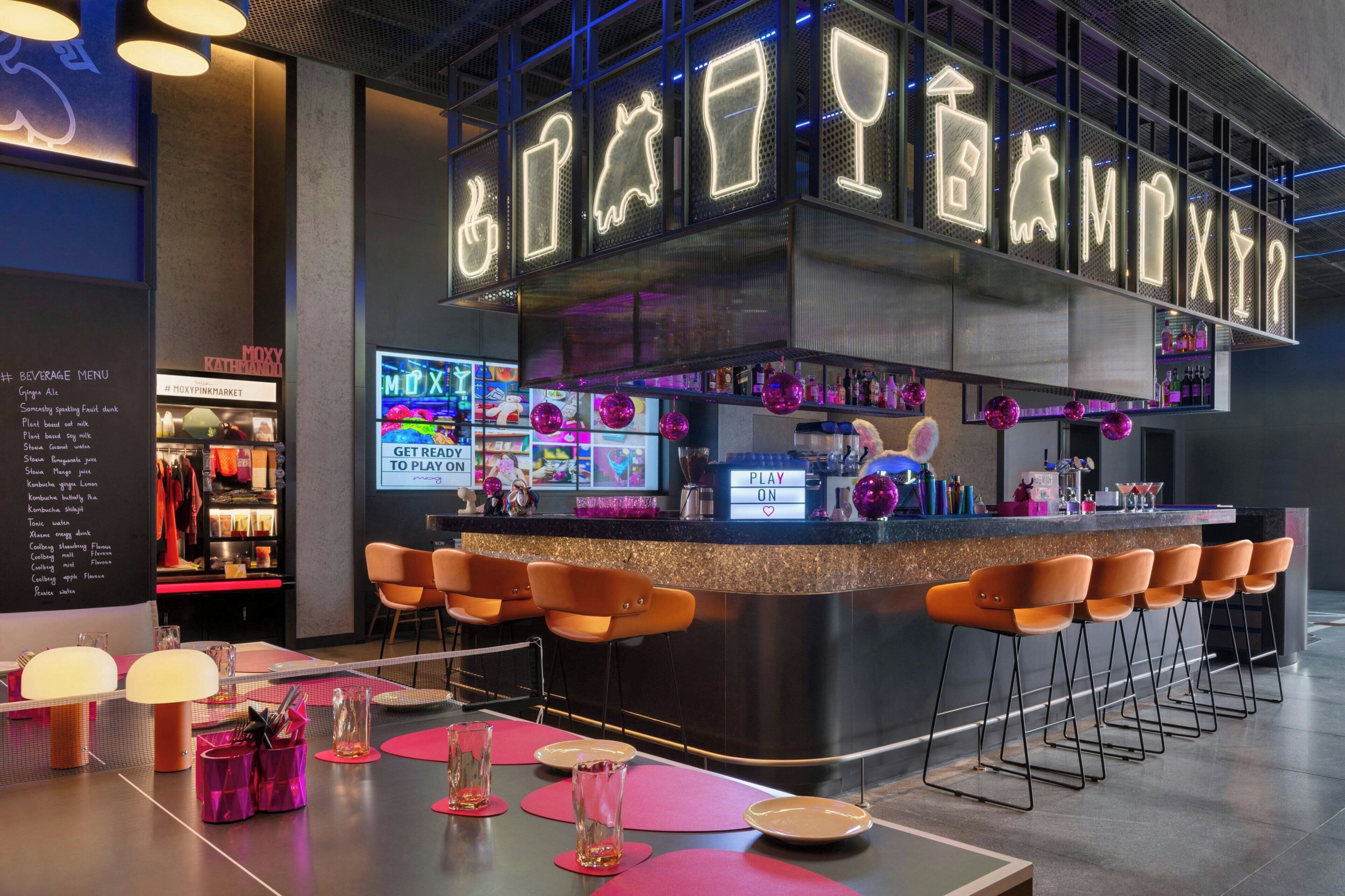A bar area with neon signs, bar stools, and a counter.
