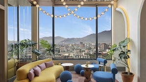 A modern living room with a city view, large windows, and comfortable seating. - Moxy Kathmandu (Kathmandu)