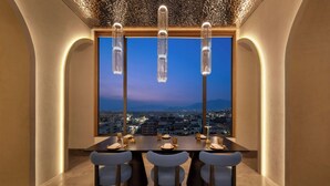 Un espace repas avec une table dressée pour quatre personnes, une vue sur la ville à travers de grandes fenêtres et un éclairage suspendu.