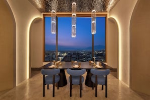 A dining area with a table set for four, a city view through large windows, and pendant lighting. - Moxy Kathmandu (Kathmandu)