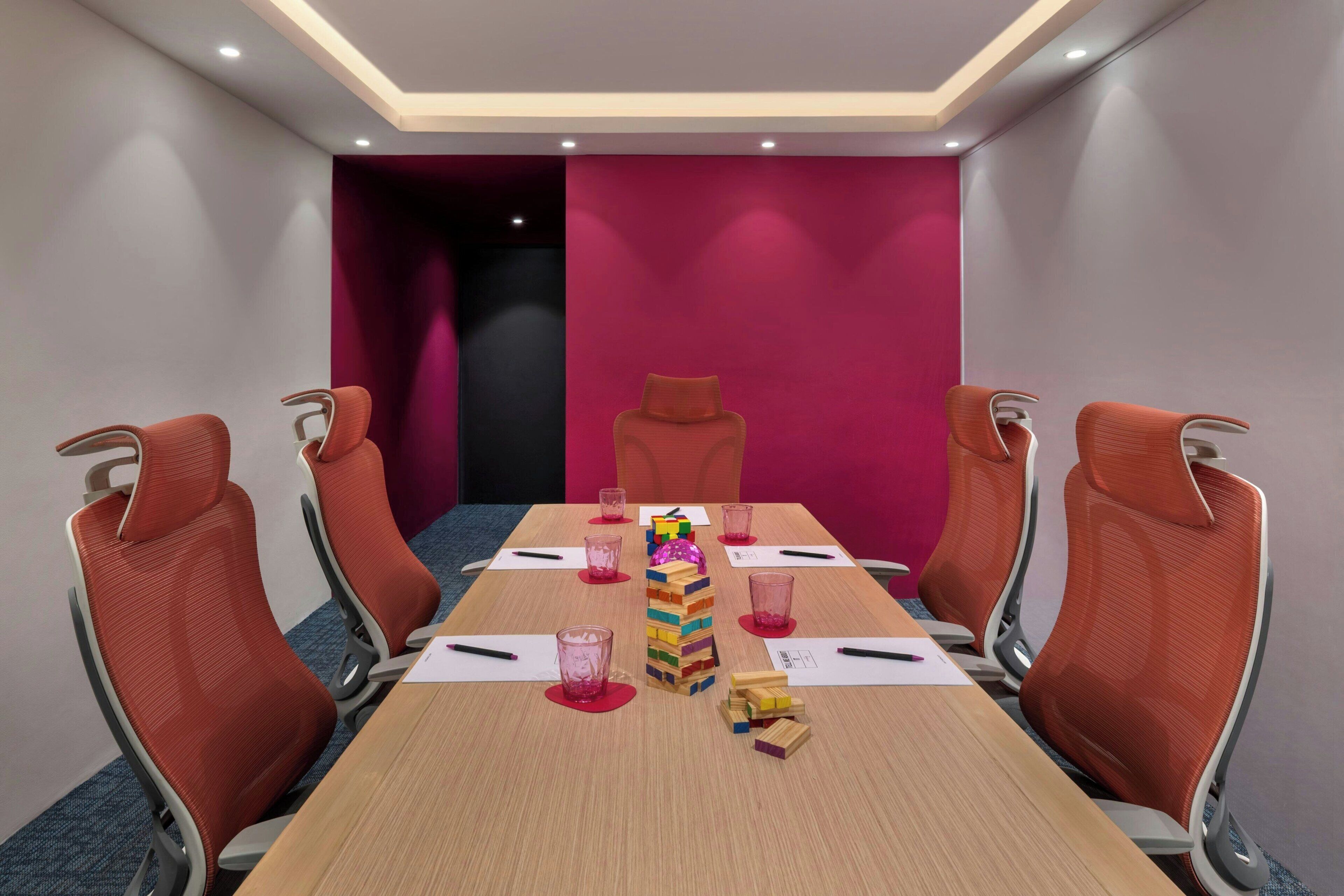 A conference room with a long table, six orange chairs, and a stack of wooden blocks.