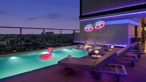 A rooftop pool with lounge chairs, a neon eye design, and a cityscape view. - Moxy Kathmandu (Kathmandu)