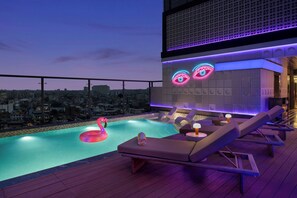 Una piscina sul tetto con poltrone relax, un motivo occhi luminosi al neon e vista sulla città.
