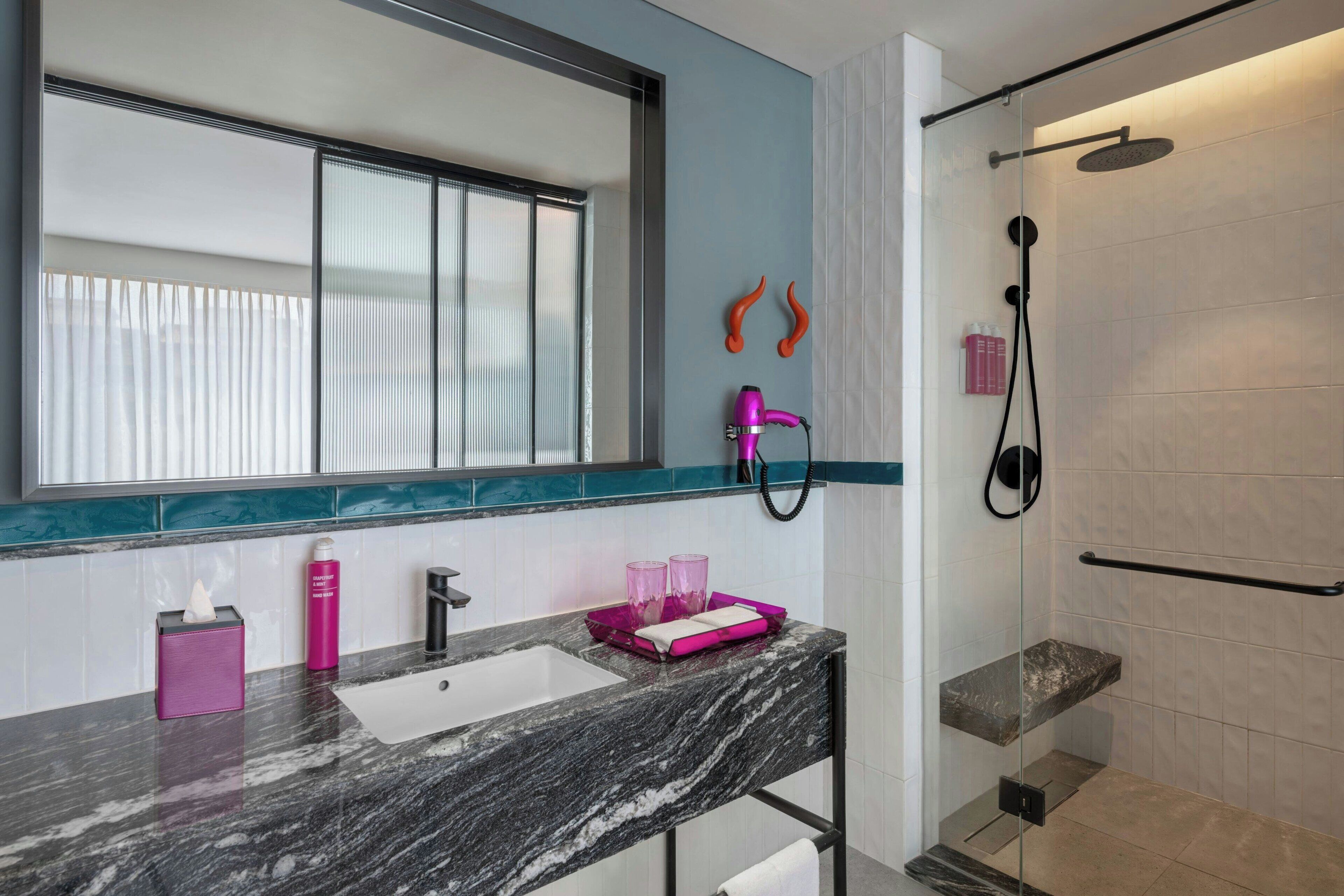 A bathroom with a large mirror, a sink, a shower, and a vanity with a marble countertop.