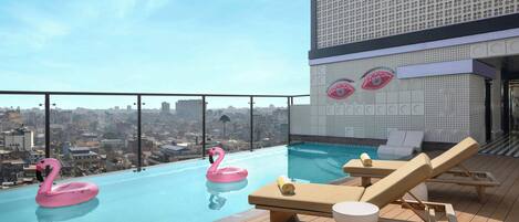 A rooftop pool with lounge chairs and two pink flamingo floats.