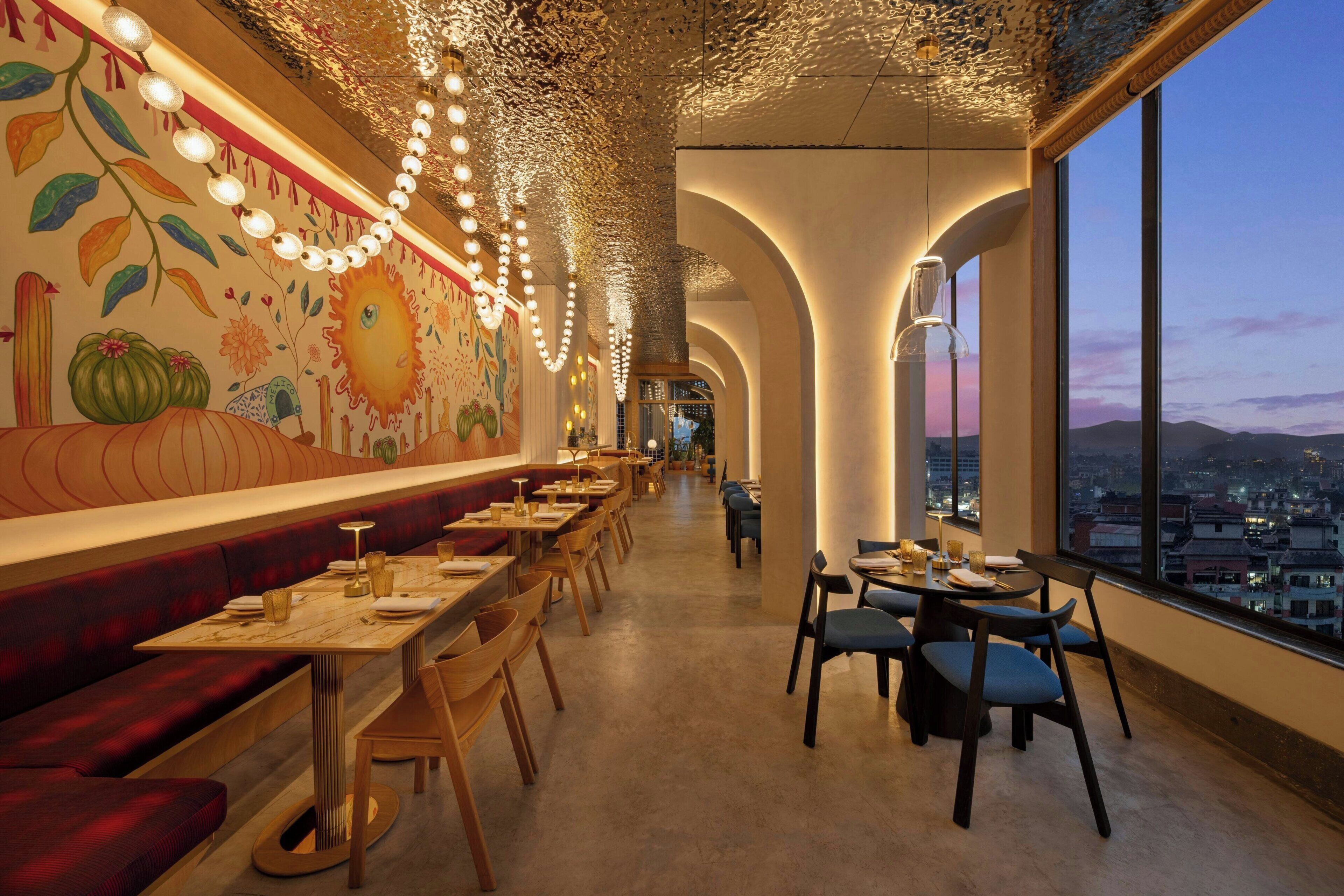 A restaurant with long communal tables, high ceilings, and a mural on the wall.
