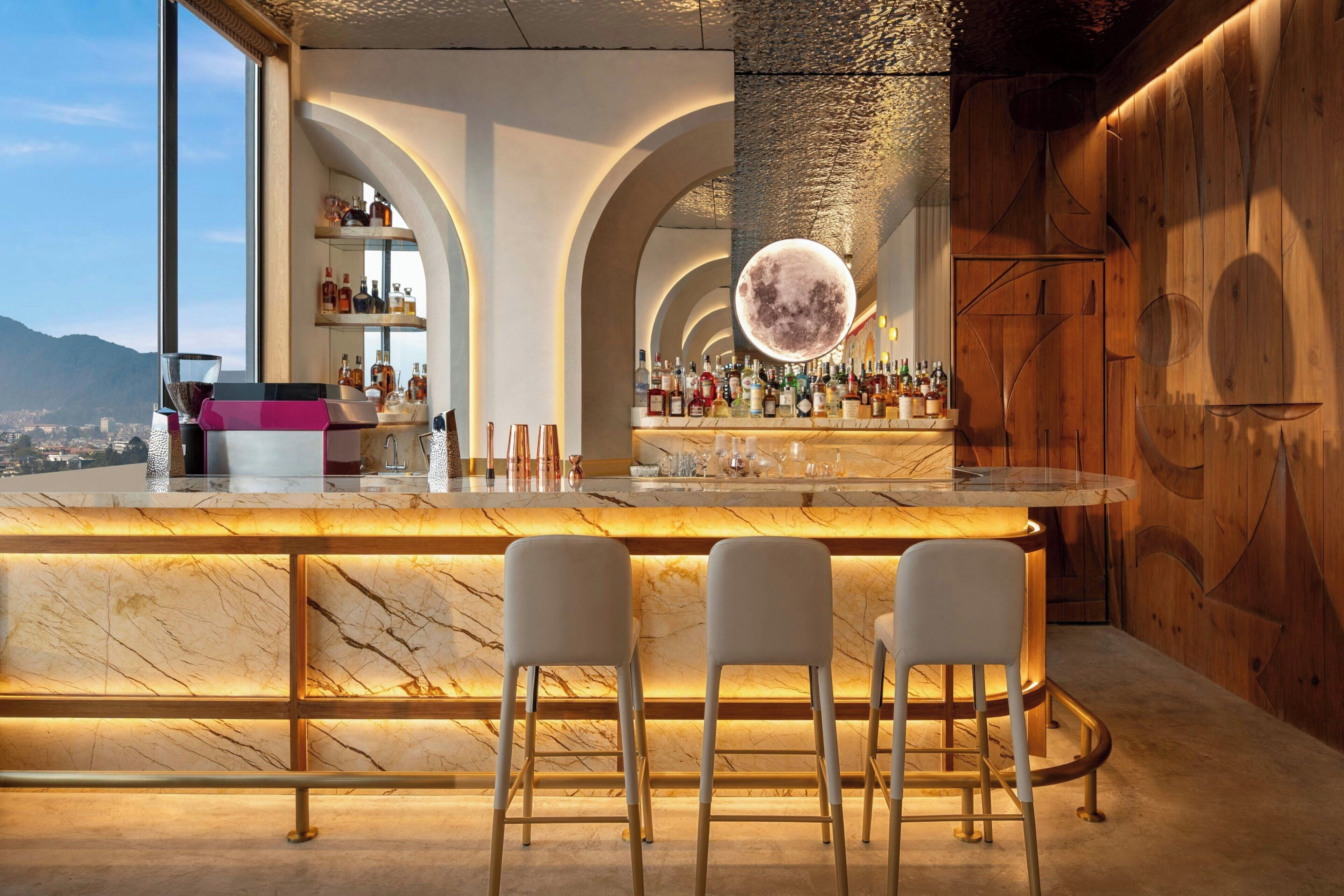 Een bar met een marmeren aanrecht, twee barstoelen en een grote lamp in de vorm van een maan.