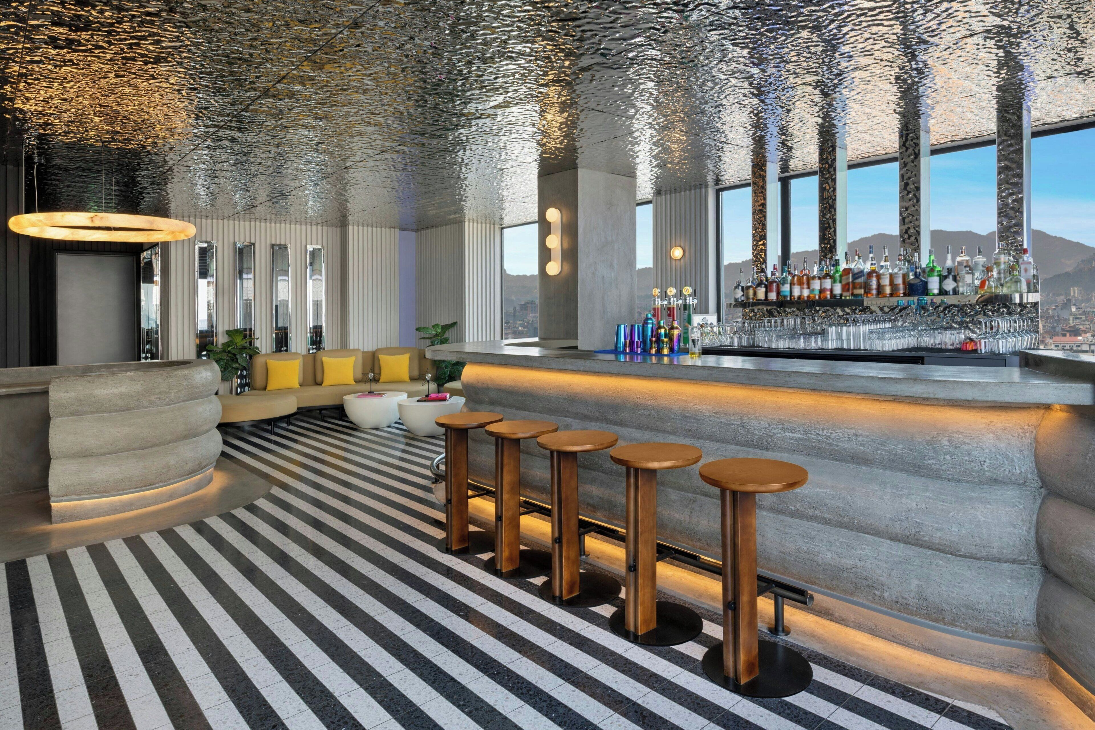 A bar area with stools, a bar counter, and a view of the cityscape through large windows.