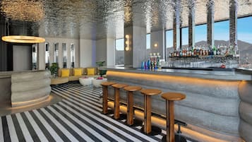 A bar area with stools, a bar counter, and a view of the cityscape through large windows.