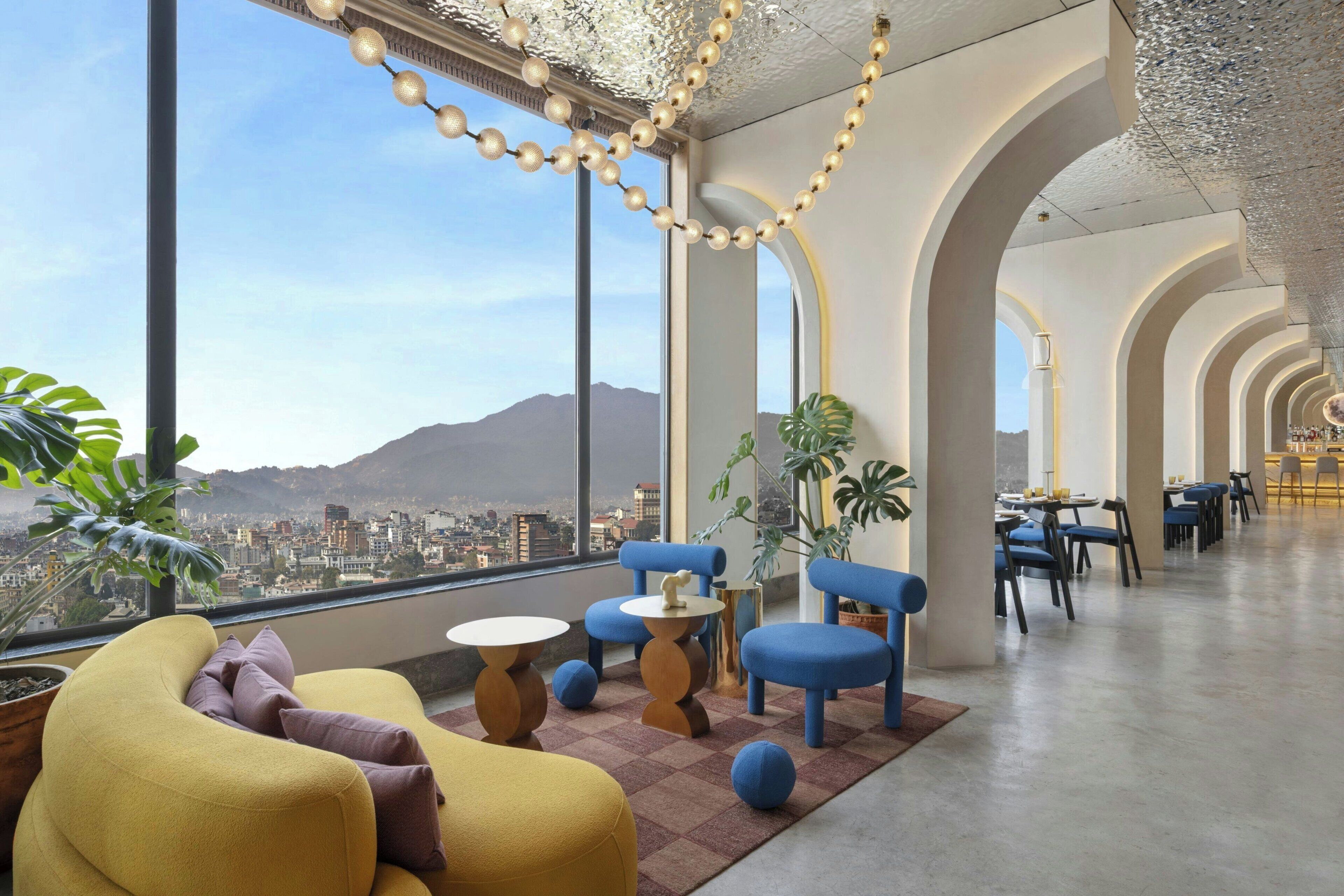 A modern interior with large windows, a seating area with round tables, and a view of a cityscape.
