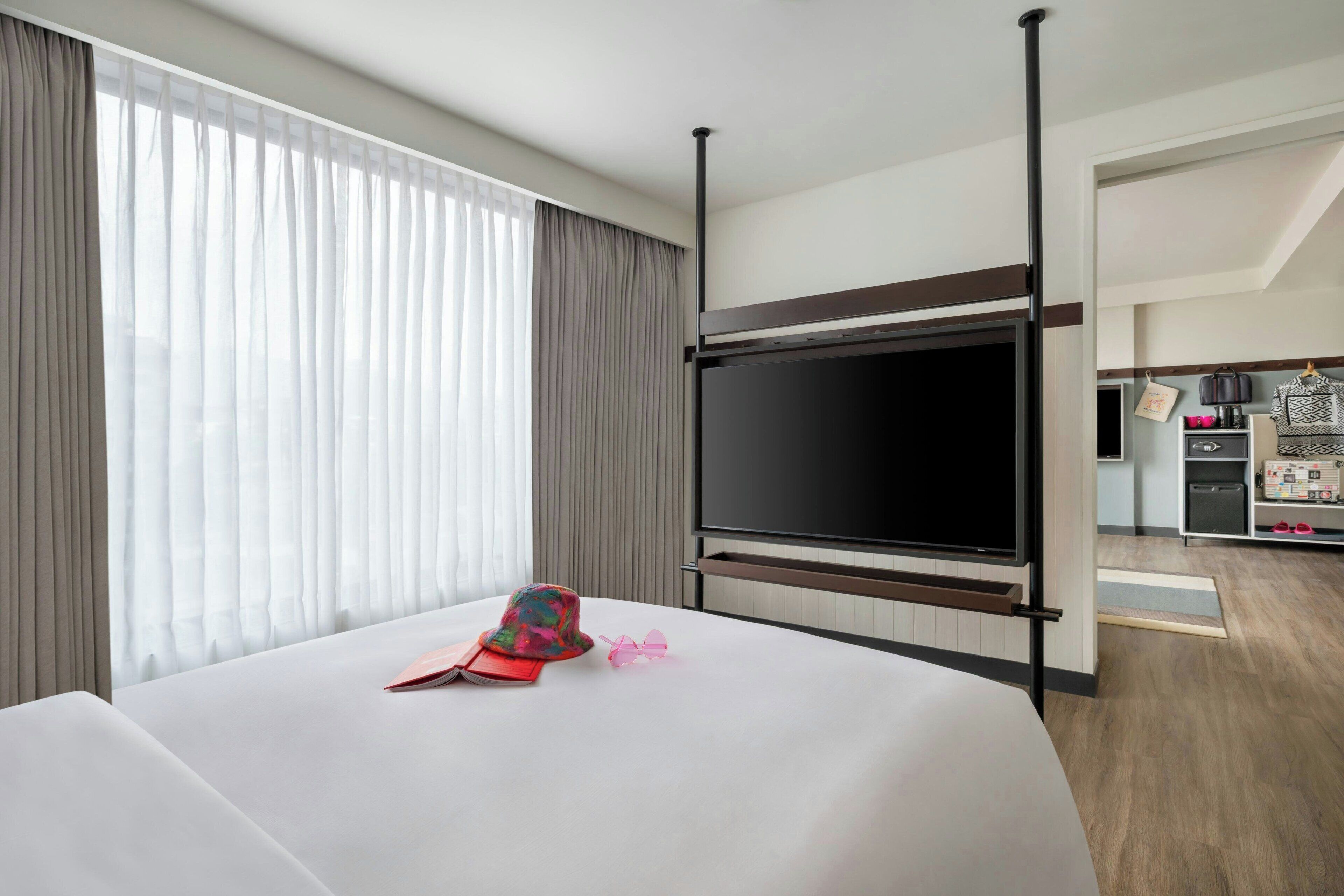 A hotel room with a large bed, a flat-screen TV, a wardrobe, and a kitchenette area.