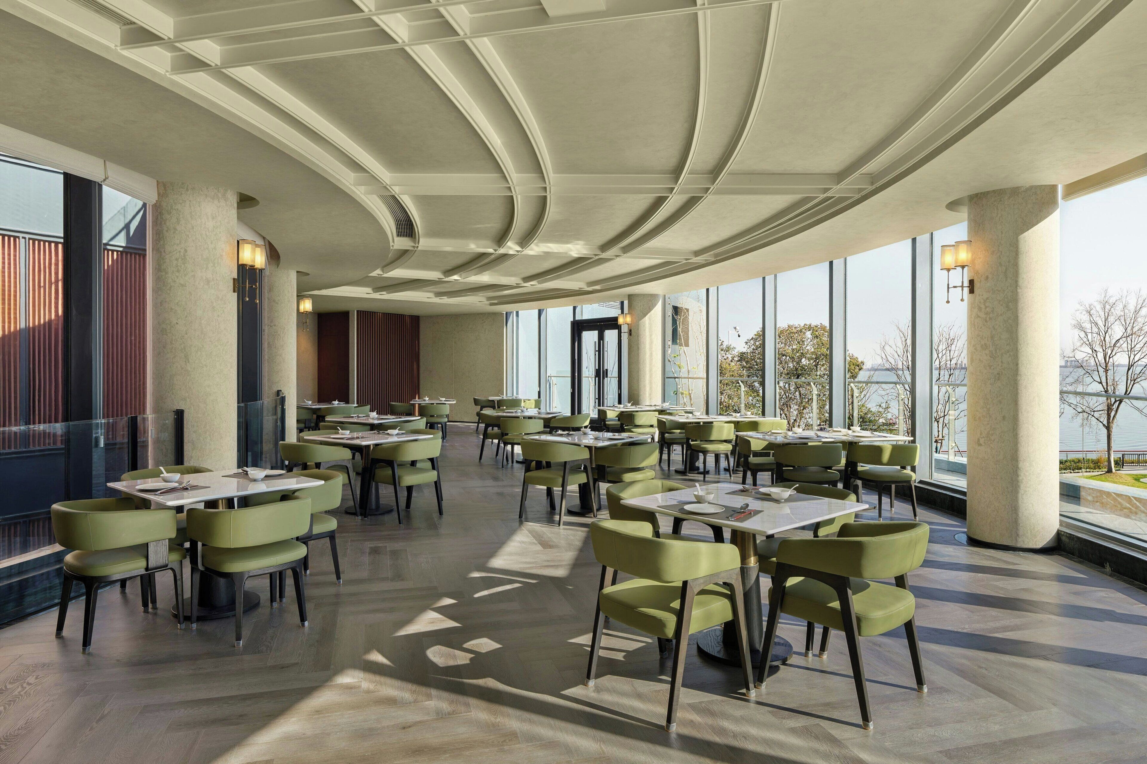 A spacious dining area with high ceilings, large windows, and modern green chairs.