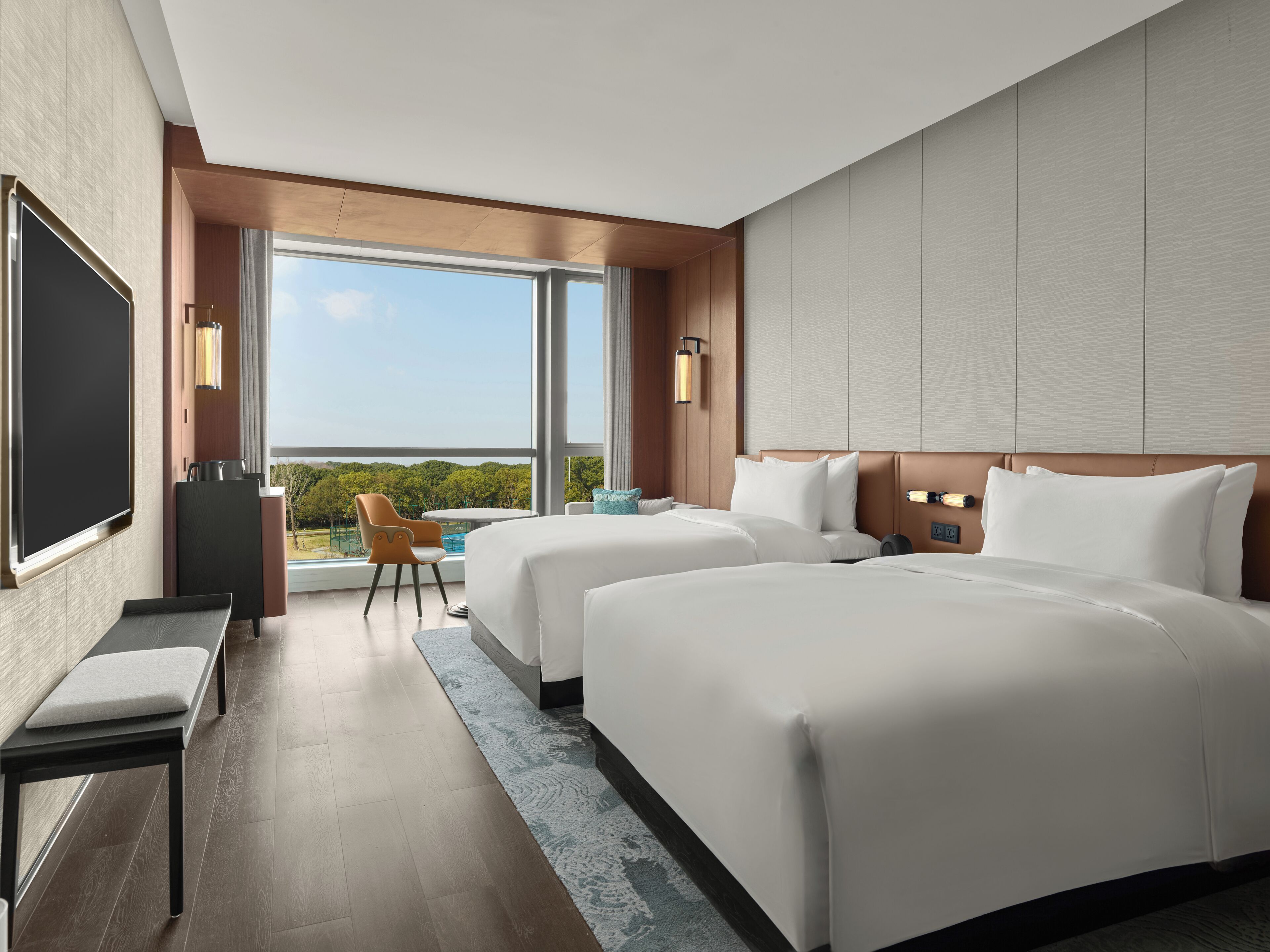 A hotel room with two beds, a TV, a desk, and a view of the outdoors.