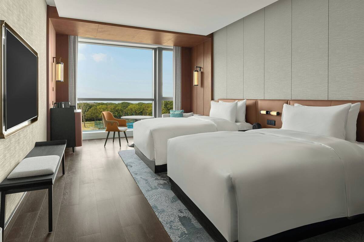 A modern hotel room with two beds, a flat-screen TV, a desk, and a chair.