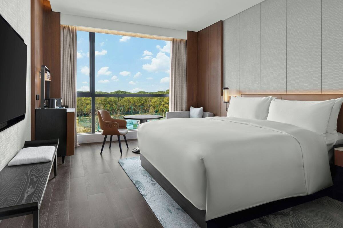 A modern hotel room with a large bed, a desk, a chair, and a TV.
