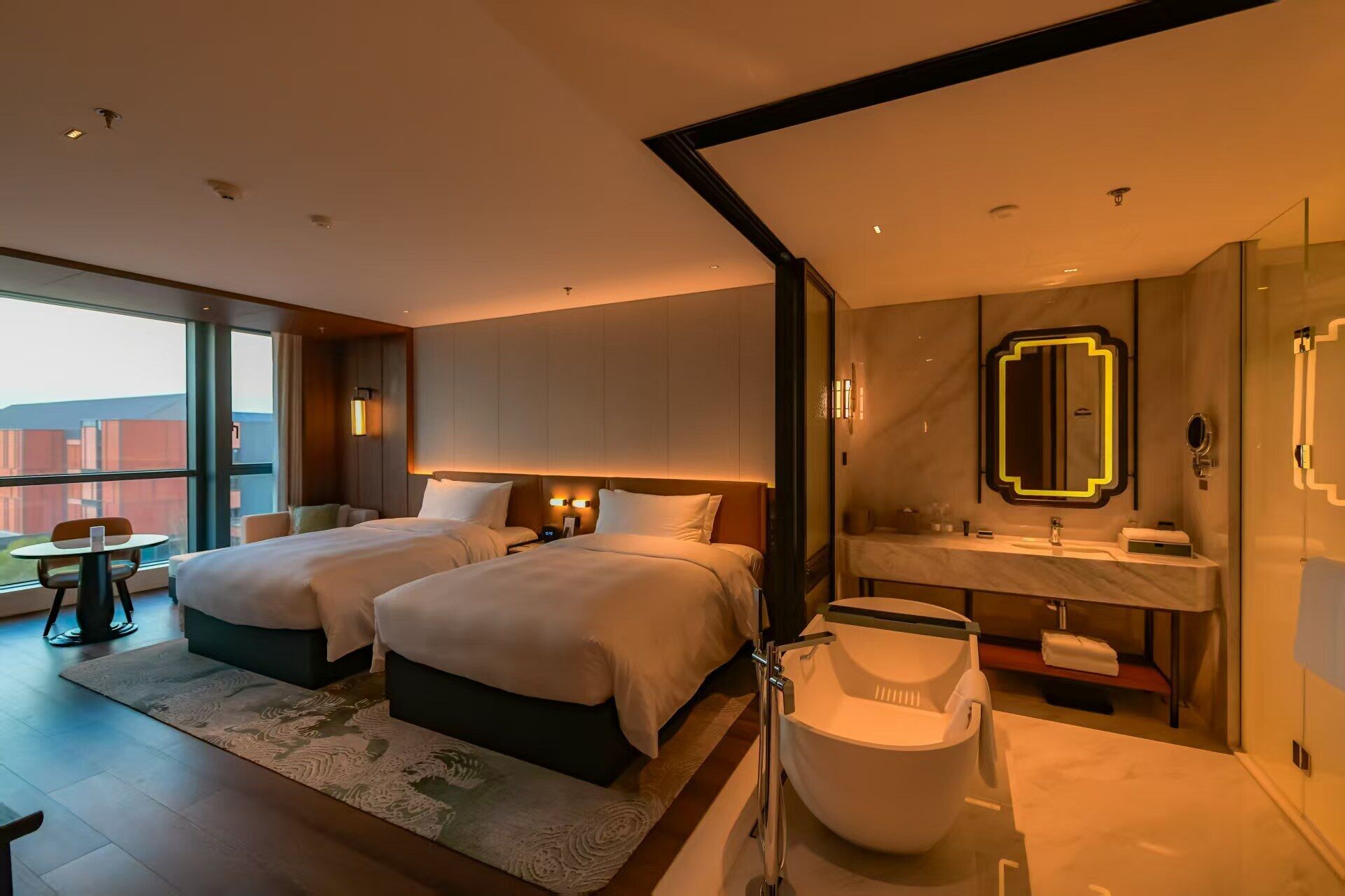 Habitación de hotel con dos camas, un ventanal grande, un baño con espejo y lavamanos.