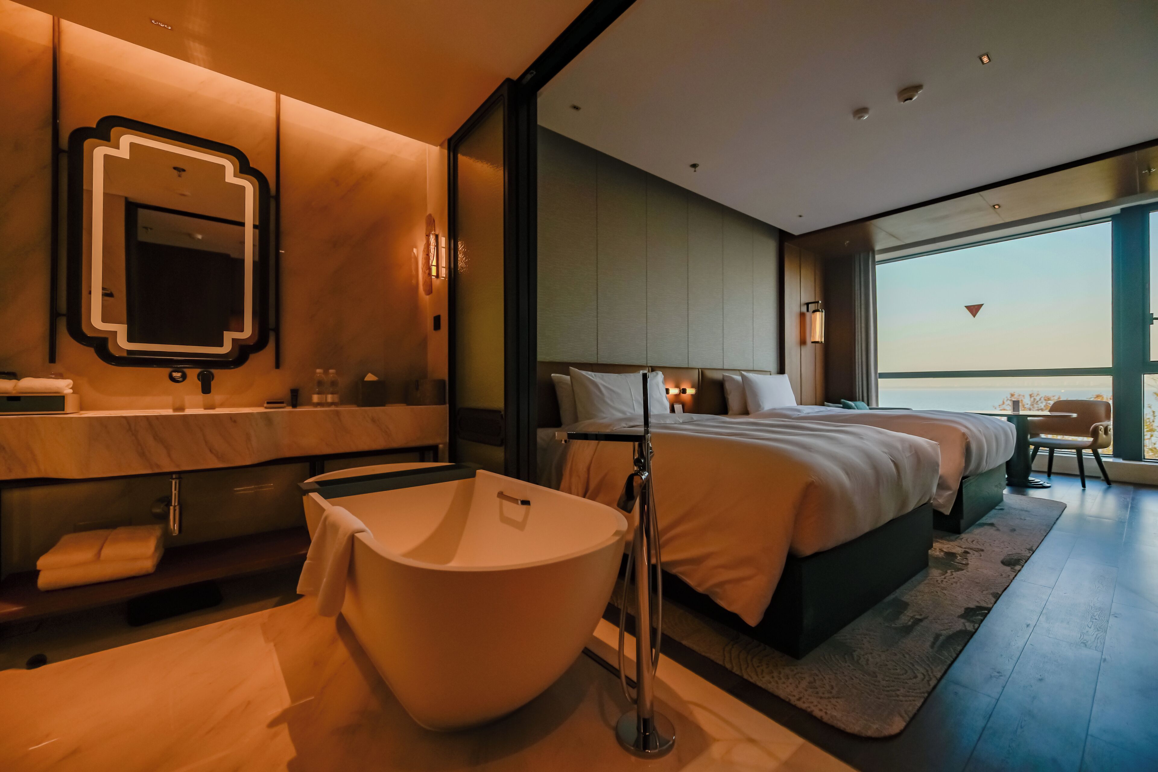 Una habitación de hotel moderna con una bañera grande, baño independiente, cama con vistas y un espejo amplio.
