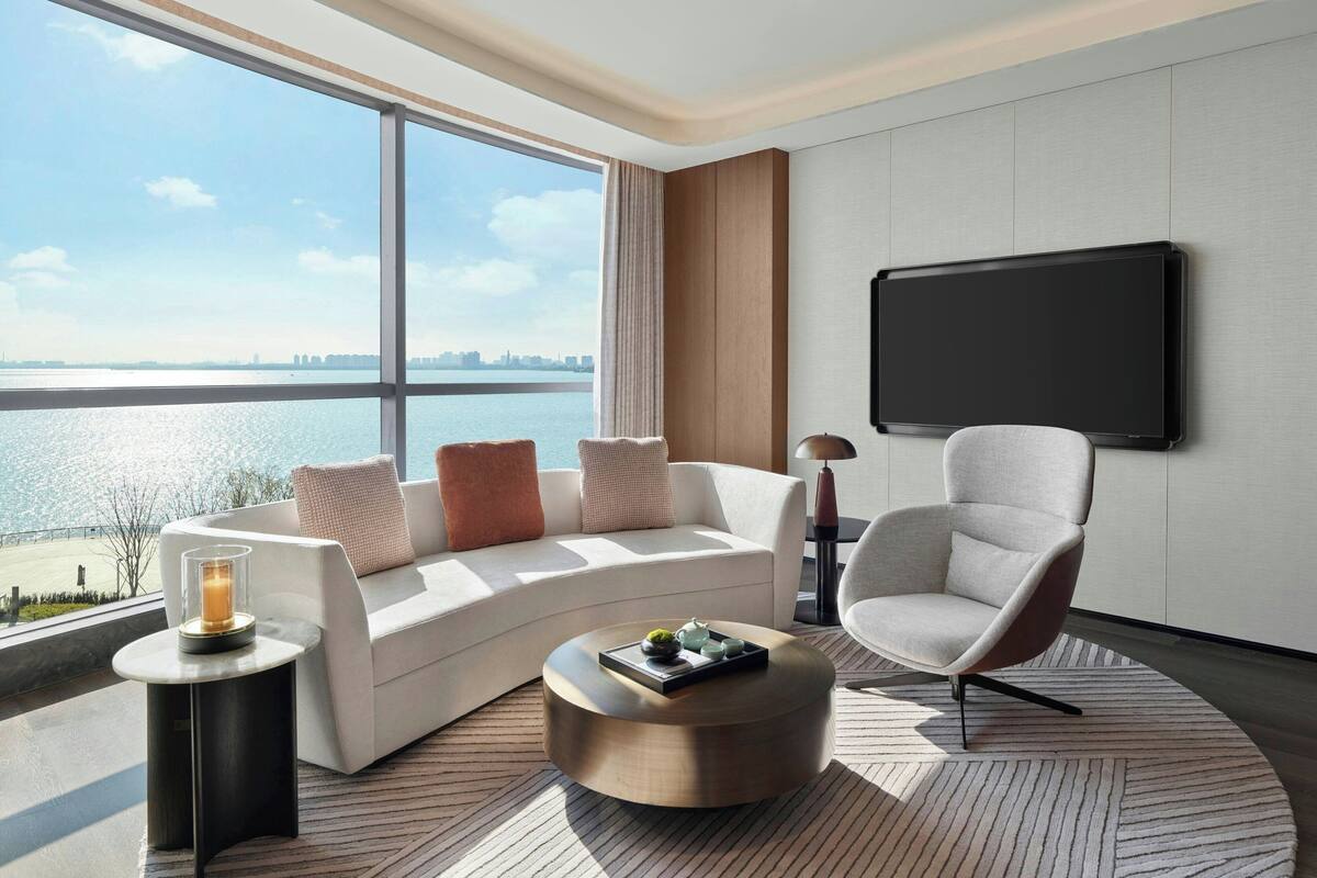 A modern hotel room with a large window offering a view of the water and city skyline.